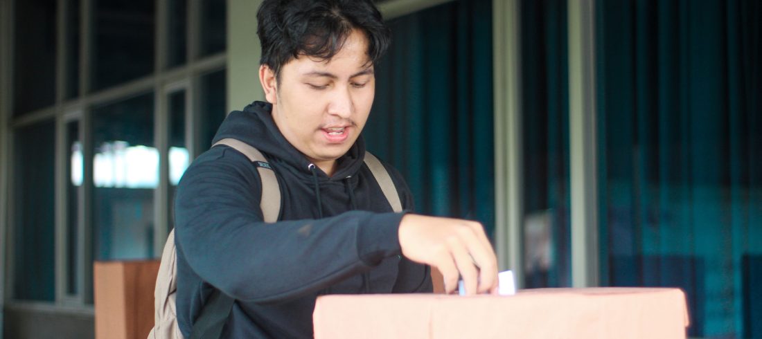 Seorang mahasiswa laki-laki memasukan pillihan dia di acara Pemilihan Mahasiswa Raya 2024
