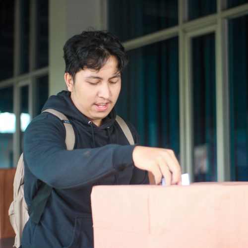 Seorang mahasiswa laki-laki memasukan pillihan dia di acara Pemilihan Mahasiswa Raya 2024