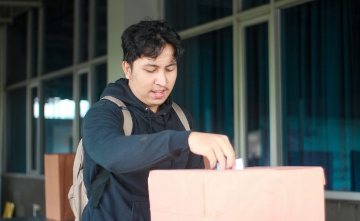 Seorang mahasiswa laki-laki memasukan pillihan dia di acara Pemilihan Mahasiswa Raya 2024